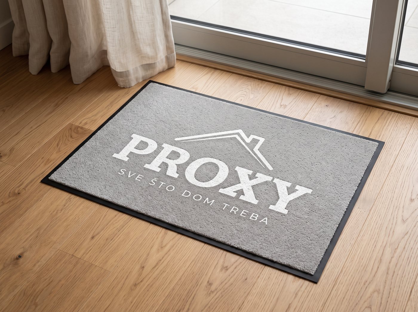Sivi otirač s bijelim logotipom na drvenom podu uz prozor